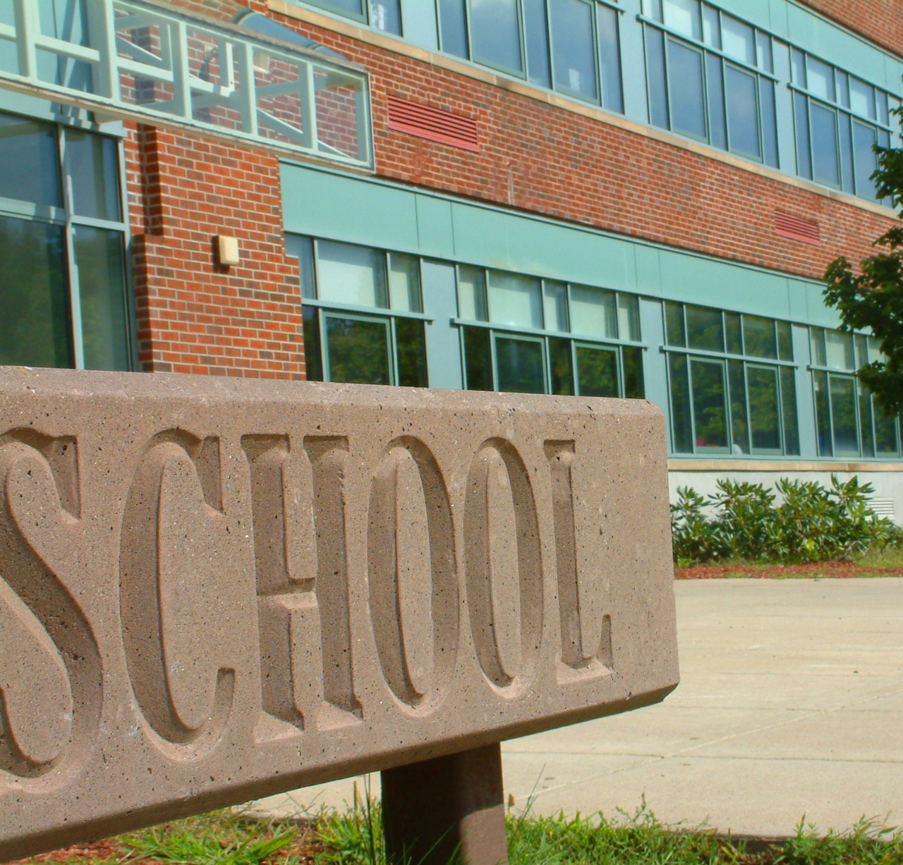 The word School prominently displayed on a sign in front of a brick school building.