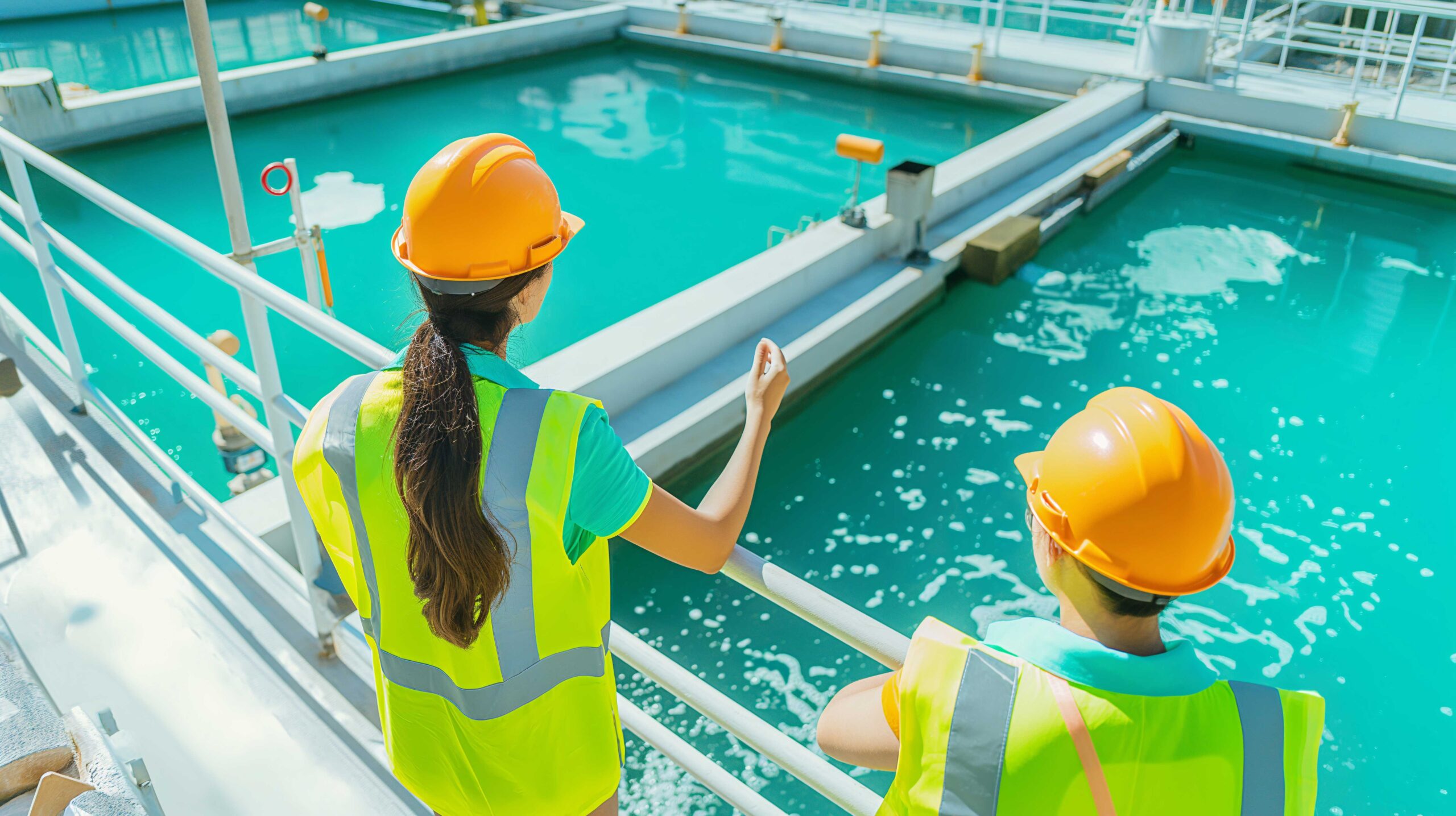 Water treatment plant undergoing maintenance with two workers overlooking a treatment pond.